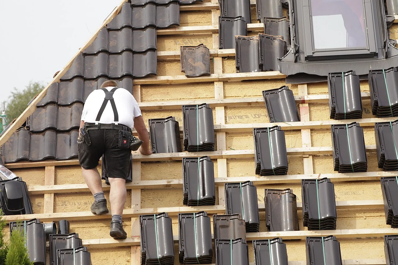 A roofer fitting interlocking tiles over exposed timber battens